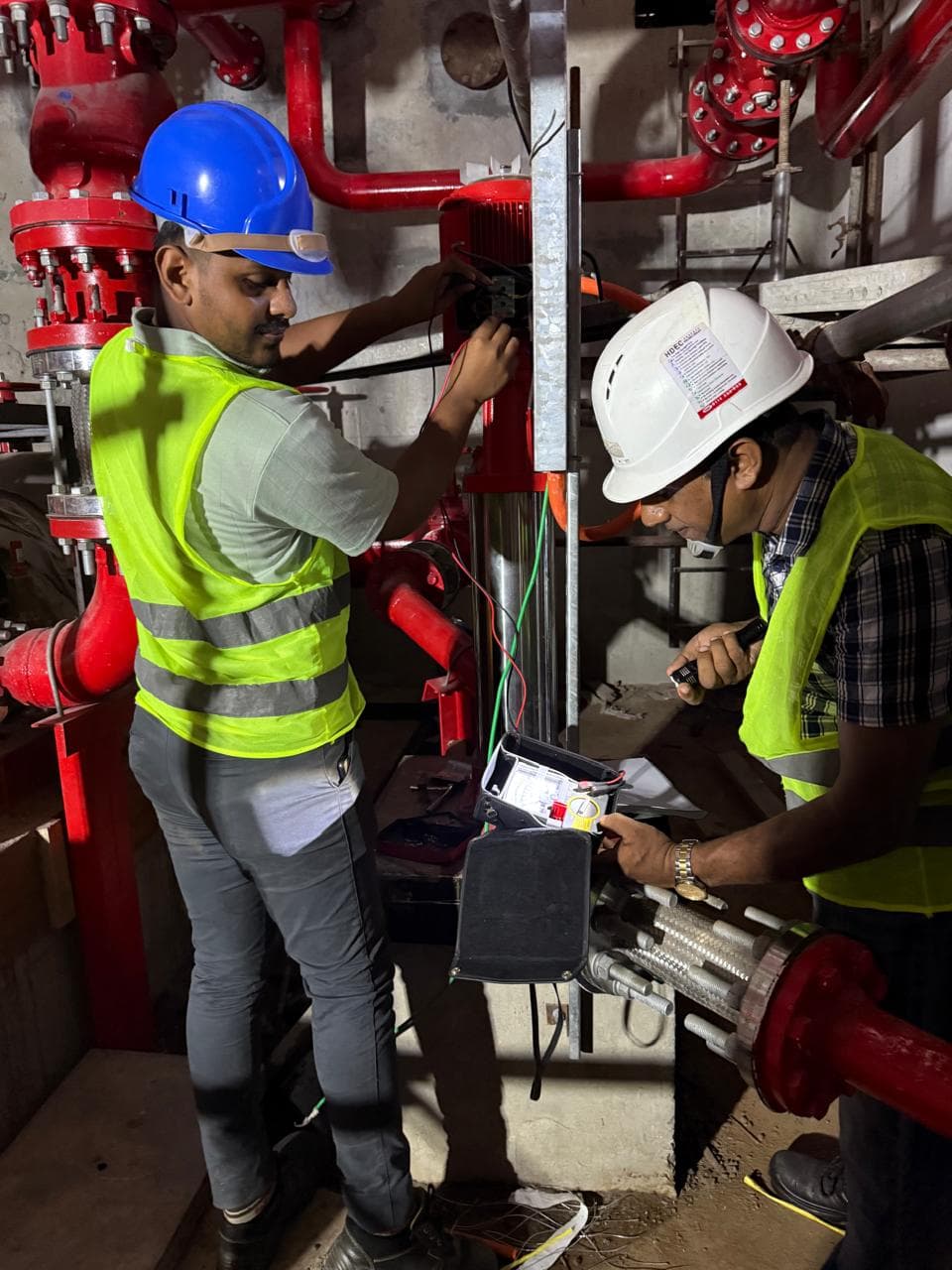 Two technicians testing fire pump equipment beside red fire protection piping